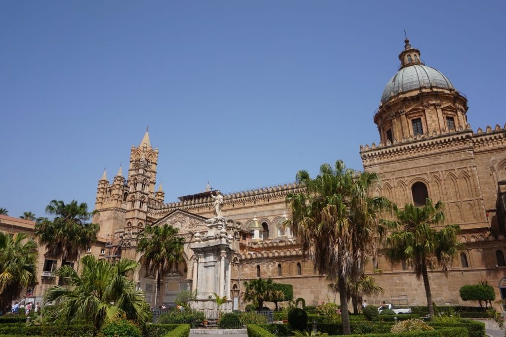 Stunning view of Palermo Cathedral with palm trees and clear blue sky in summer.