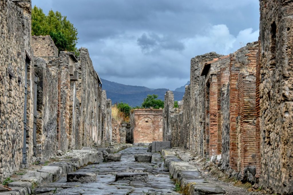 Explore the ancient stone ruins and streets of Pompeii, Campania with distant mountains under a cloudy sky.